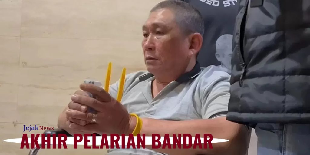 Tersangka Erwin Iskandar alias Koko Erwin dengan pengawalan ketat personil bersenjata lengkap saat tiba di Bandara Soekarno-Hatta menggunakan kursi roda pasca penangkapan di Tanjung Balai.