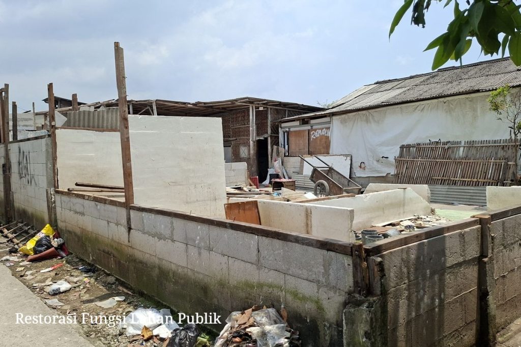 Alat berat ekskavator sedang meratakan bangunan semi-permanen di lahan TPU Kamal Kalideres dengan pengawalan ketat petugas gabungan.