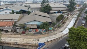 Alat berat dan pekerja konstruksi sedang meratakan material semen pada satu sisi lajur jalan raya.